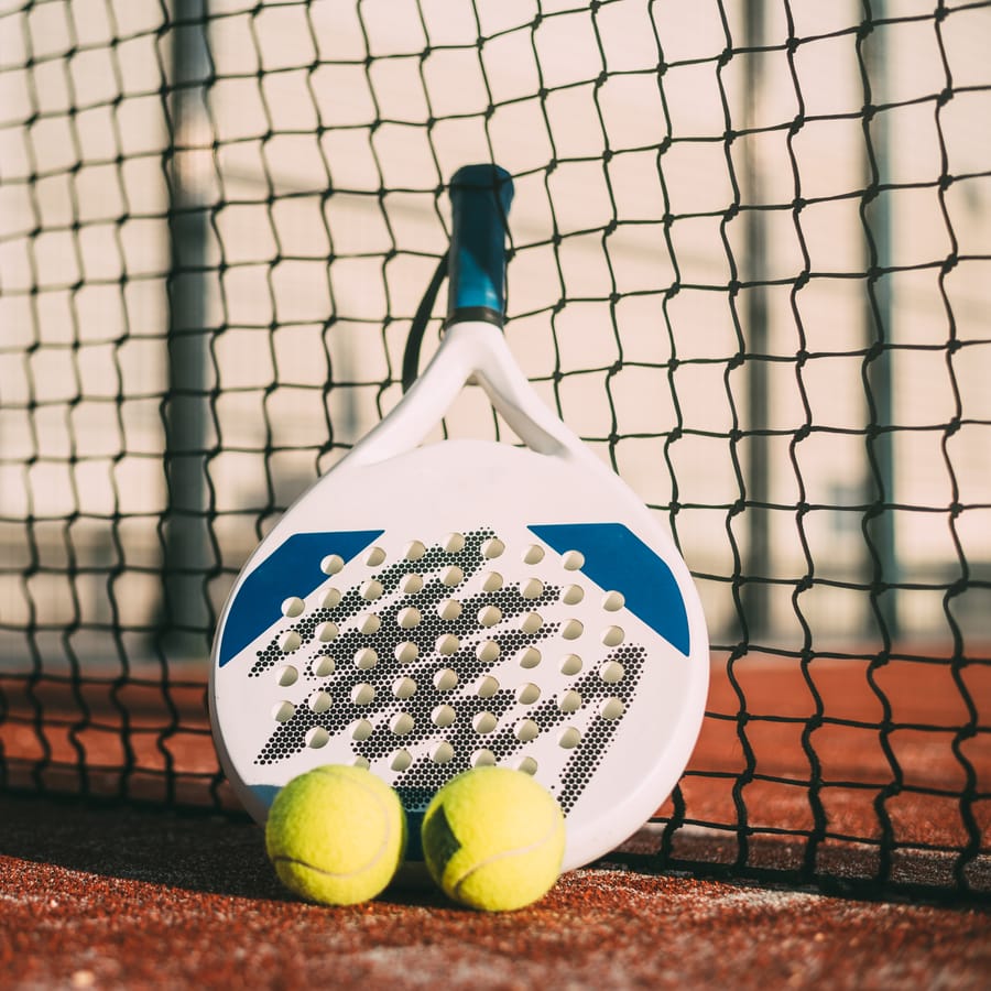 Padel racket resting against the net with balls
